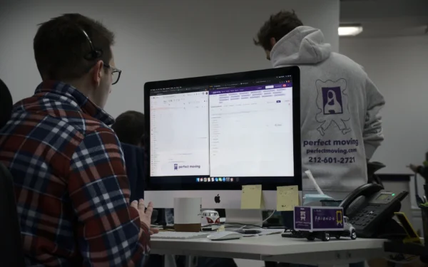 A Perfect Moving office worker in a headset at a computer, a coworker in a company hoodie behind